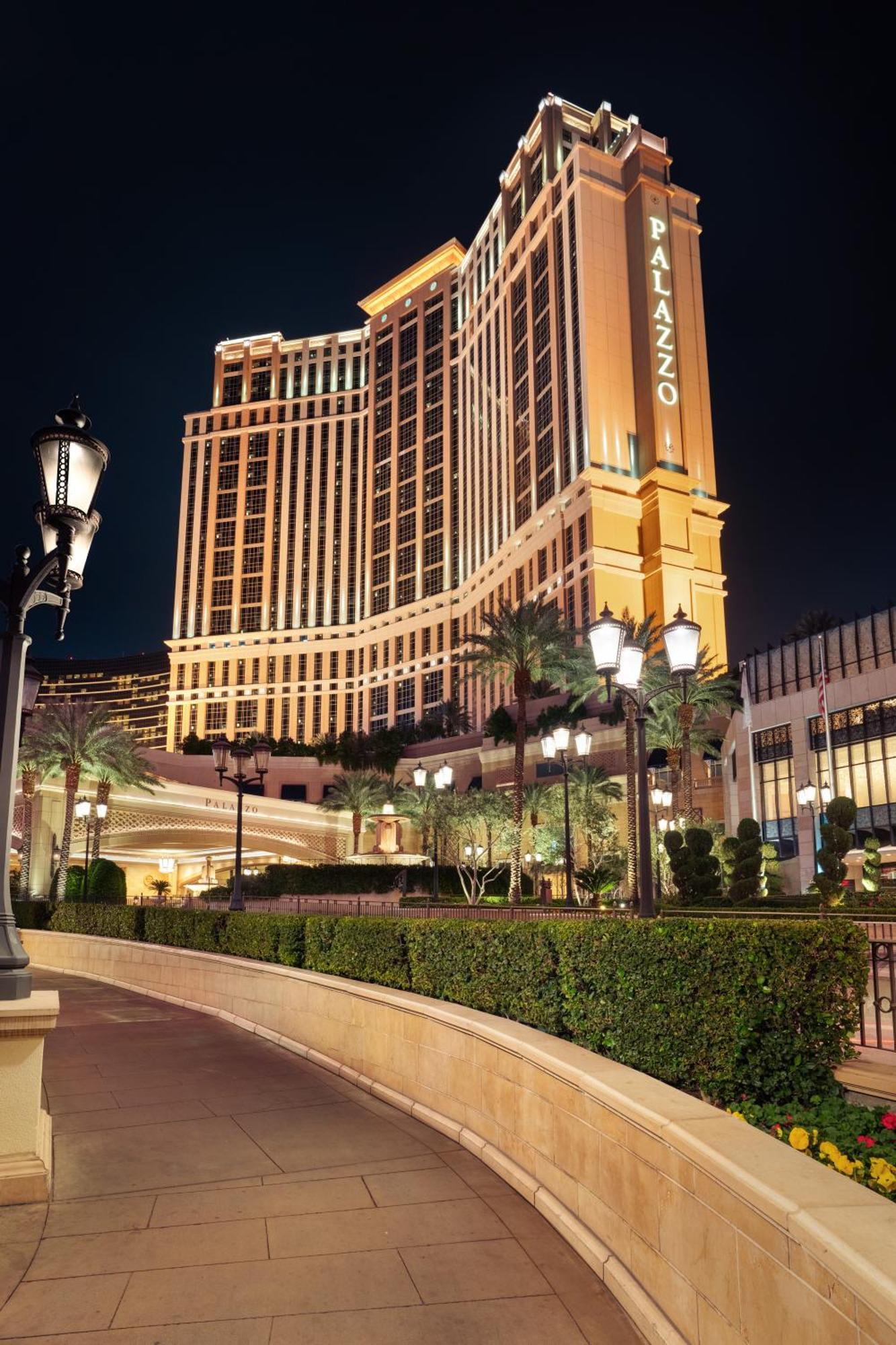 Hotel The Palazzo At The Venetian Las Vegas Exterior foto The photo depicts a large, illuminated hotel building at night. The architecture is modern and elegant, featuring tall structures with decorative lighting. Surrounding the hotel are neatly trimmed hedges and palm trees, contributing to a luxurious at